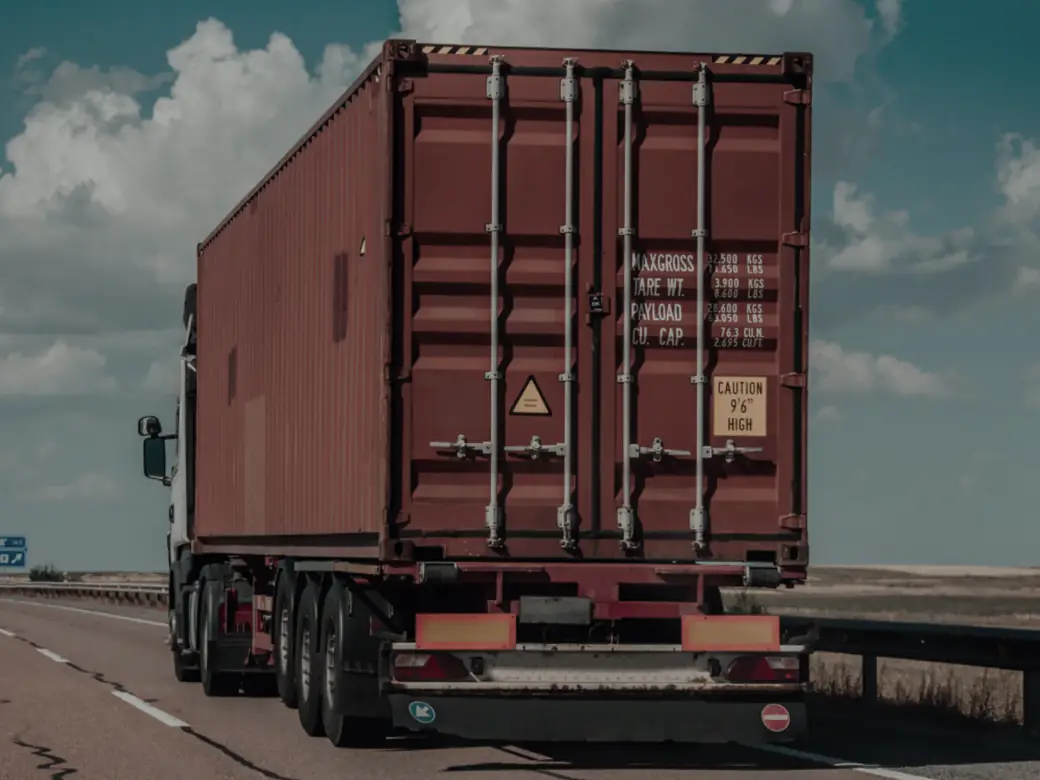 A shipping container on a trailer, seen from behind on a main road