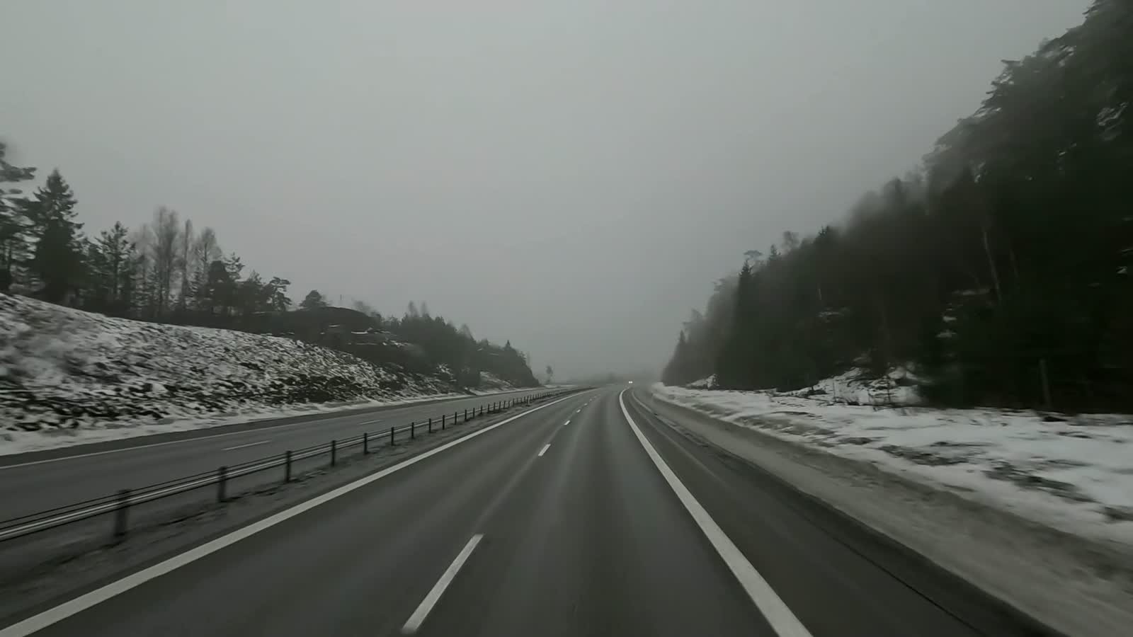 Driver's view of a snow-covered motorway running through Swedish forest in winter